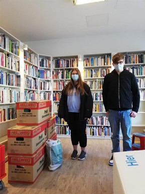 Eine Schülerin und ein Schüler stehen in den Räumen von Bodo mit fünf Umzugskartons mit Spenden.